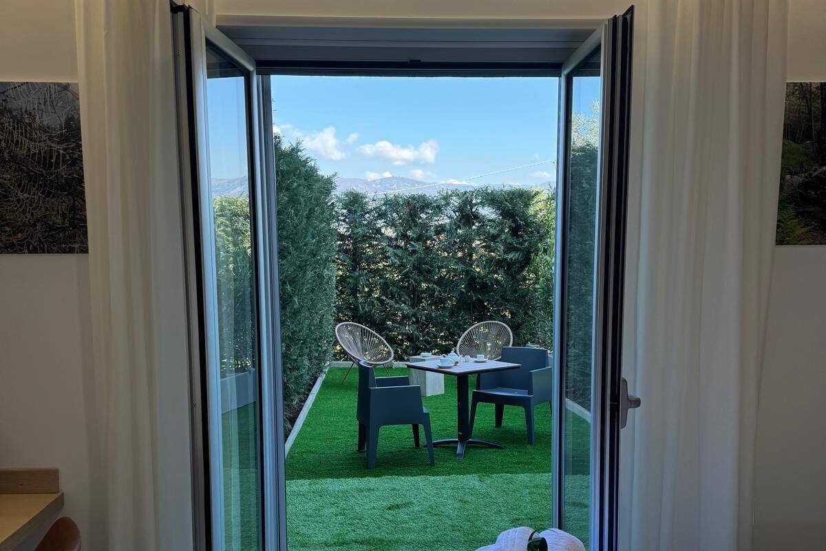 A hotel room with a bed, a desk, and a view of an outdoor area with a table and chairs.