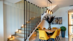 A modern dining area with a staircase, a dining table with yellow chairs, and a vase with decorative plants. - Villa Grand Blue (Hersonissos)