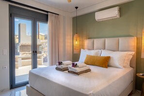 A hotel room with a bed, a nightstand, an air conditioning unit, and a view through a sliding door. - Villa Grand Blue (Hersonissos)