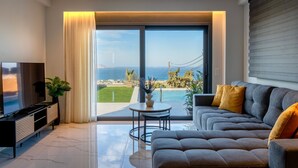 A modern living room with a large TV, sofa, and a view of the sea. - Villa Grand Blue (Hersonissos)