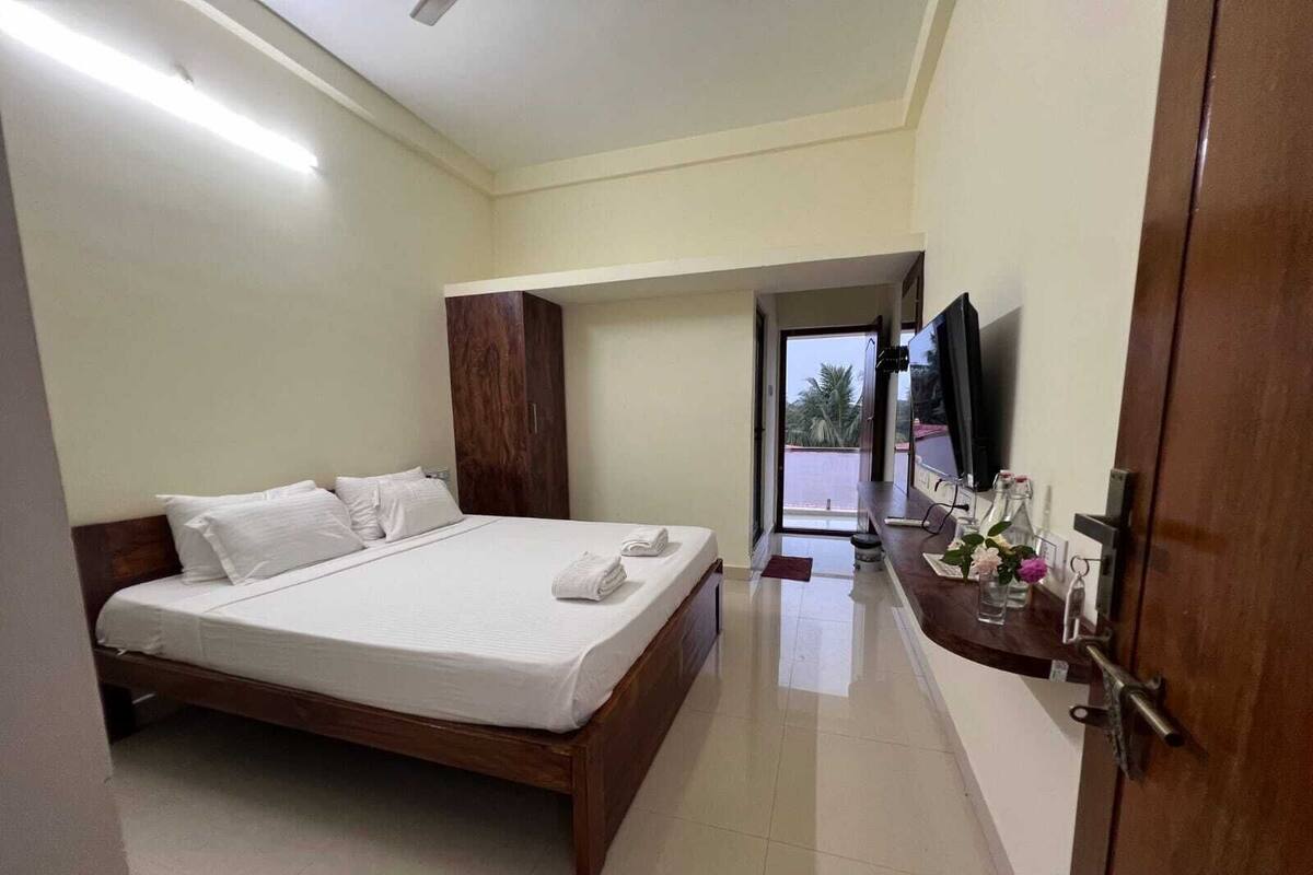 Een hotelkamer met een groot bed, een houten garderobe, een televisie op een standaard en een zichtbare badkamer door een geopende deur.