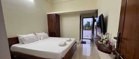 A hotel room with a large bed, a wooden wardrobe, a TV on a stand, and a bathroom visible through an open door.