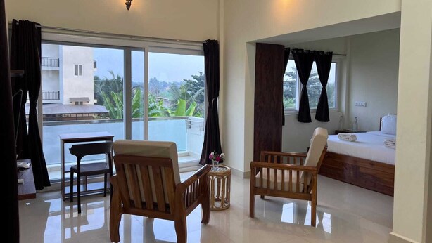 A spacious room with a balcony, a bed, and two wooden chairs. - Gold Mountain Wellness Resort (Tiruvannamalai)