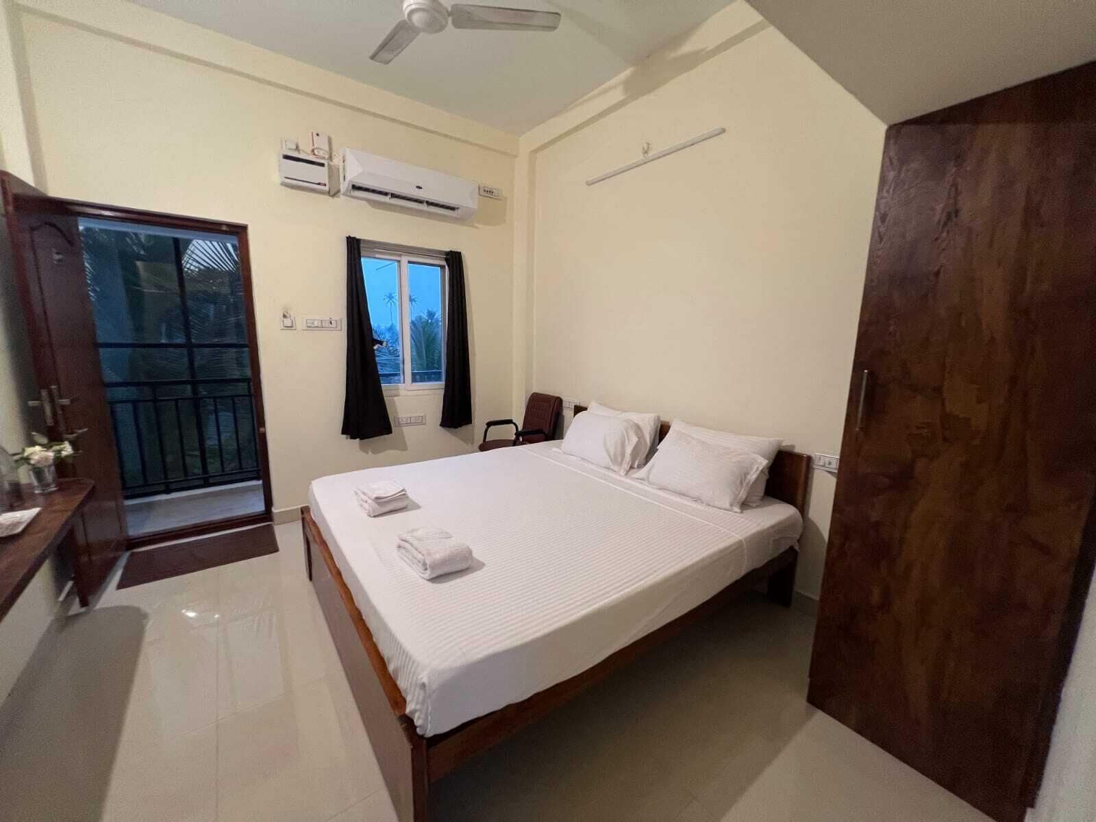 Un dormitorio con cama, armario, escritorio, aire acondicionado y ventana con cortinas.