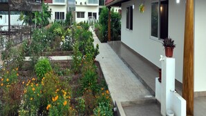 A residential building with multiple floors, balconies, and a garden area with various plants and flowers. - Gold Mountain Wellness Resort (Tiruvannamalai)