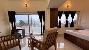 A hotel room with a bed, a wooden bench, a small table with a vase, and a view of the outside. - Gold Mountain Wellness Resort (Tiruvannamalai)