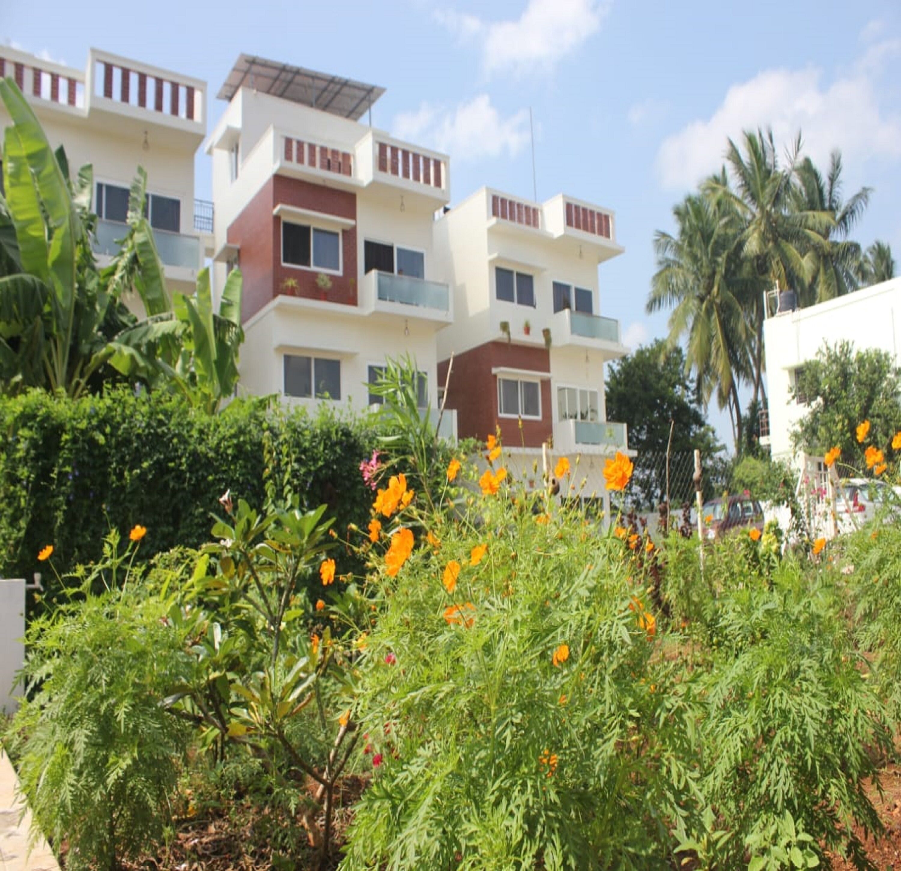 Un edificio residencial de varios pisos con balcones, rodeado de vegetación exuberante y plantas con flores.