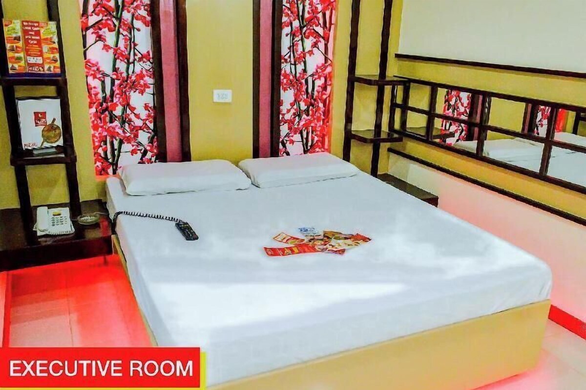 Una habitación ejecutiva con una cama, una mesita de noche con un teléfono y un estante con objetos.