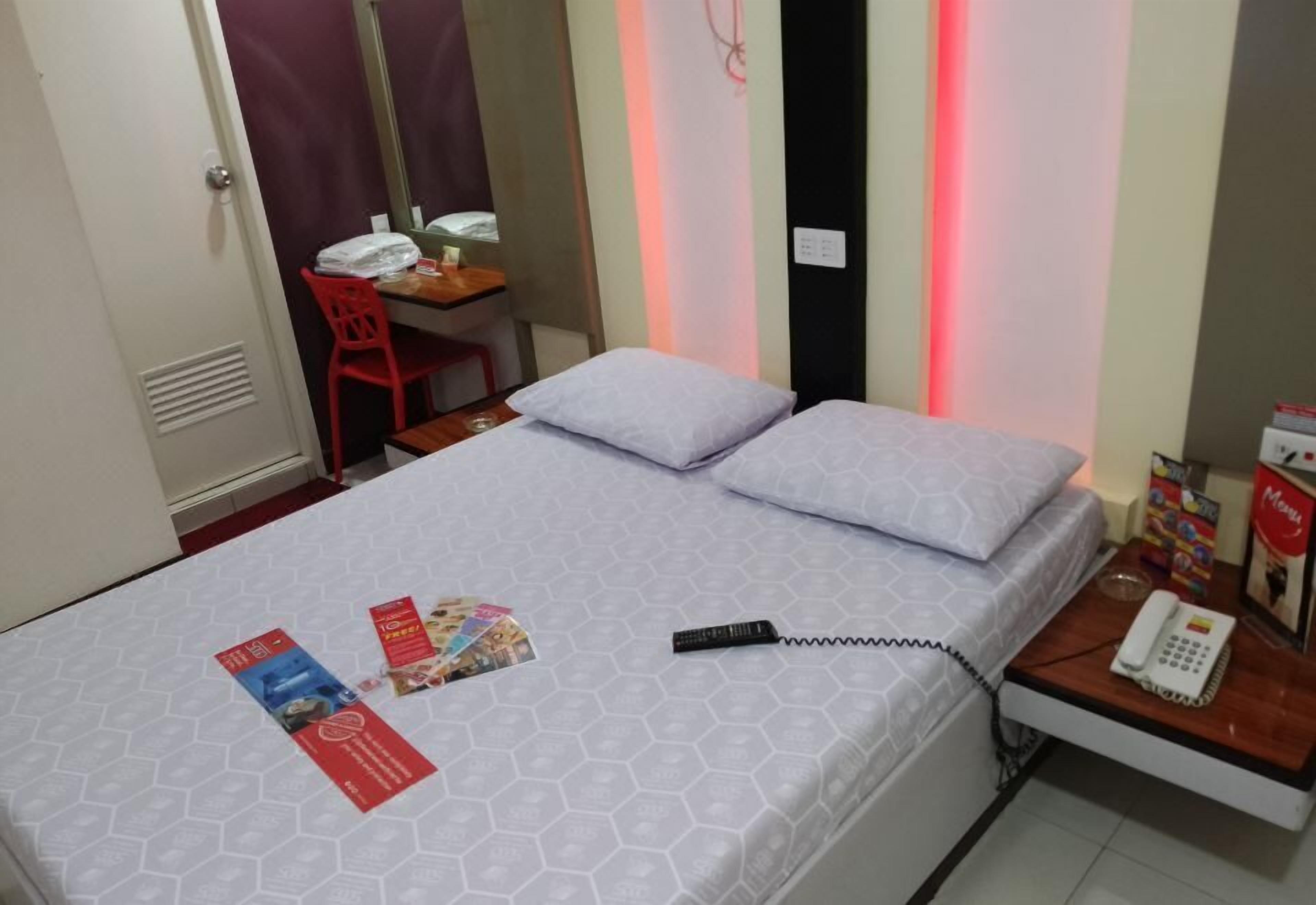 A hotel room with a bed, a desk with a chair, a telephone, and a wall-mounted mirror.