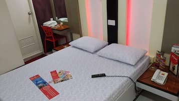 A hotel room with a bed, a desk with a chair, a telephone, and a wall-mounted mirror.