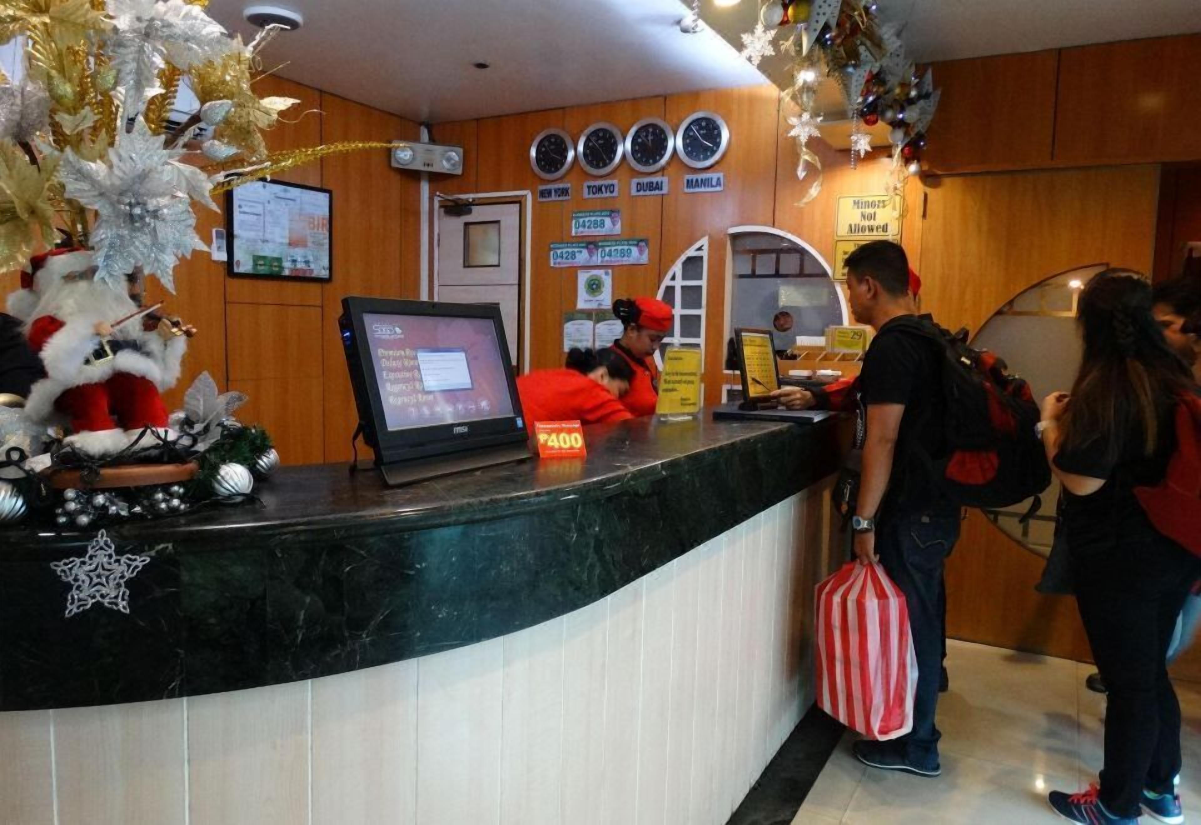 Bancada de recepção de hotel com tela digital, relógios e aviso indicando que menores não são permitidos.