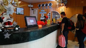 Bancada de recepção de hotel com tela digital, relógios e aviso indicando que menores não são permitidos.