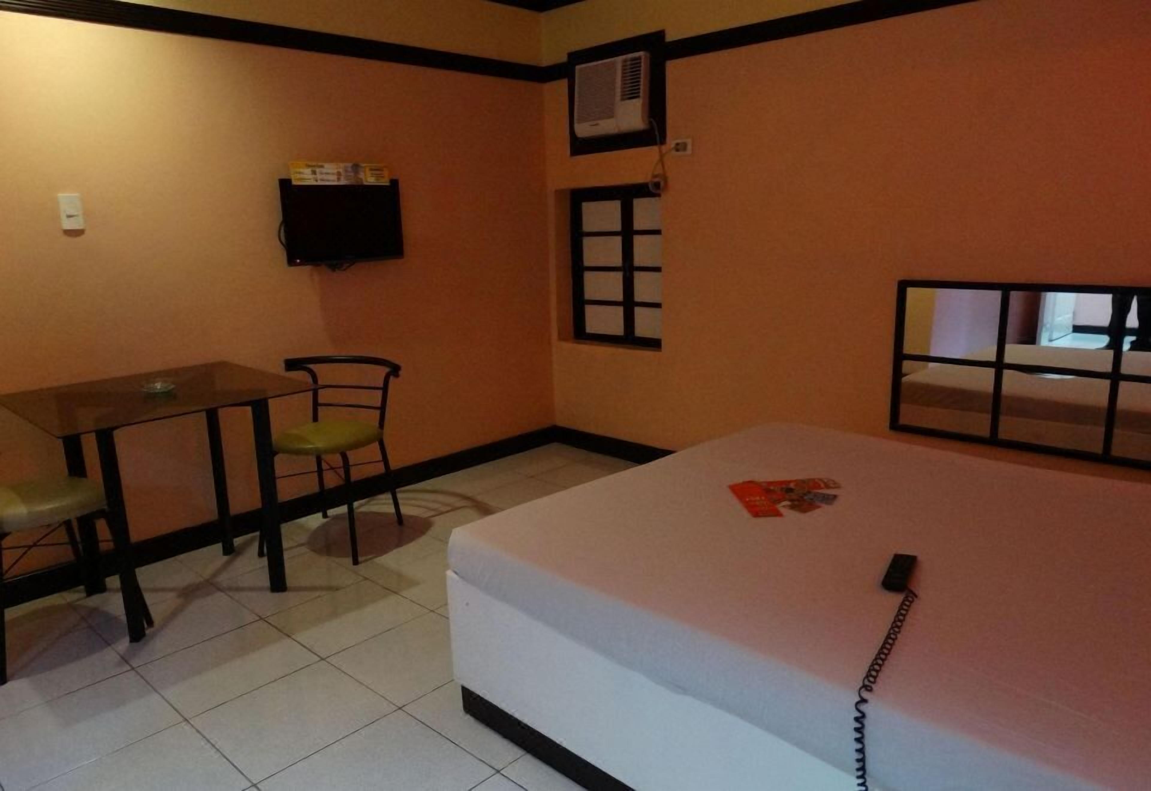 Una stanza con un letto, un tavolo, due sedie, una televisione e una finestra.