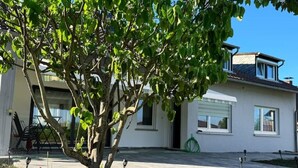 Una casa moderna con un porche cubierto, un árbol en primer plano y un cielo azul despejado.