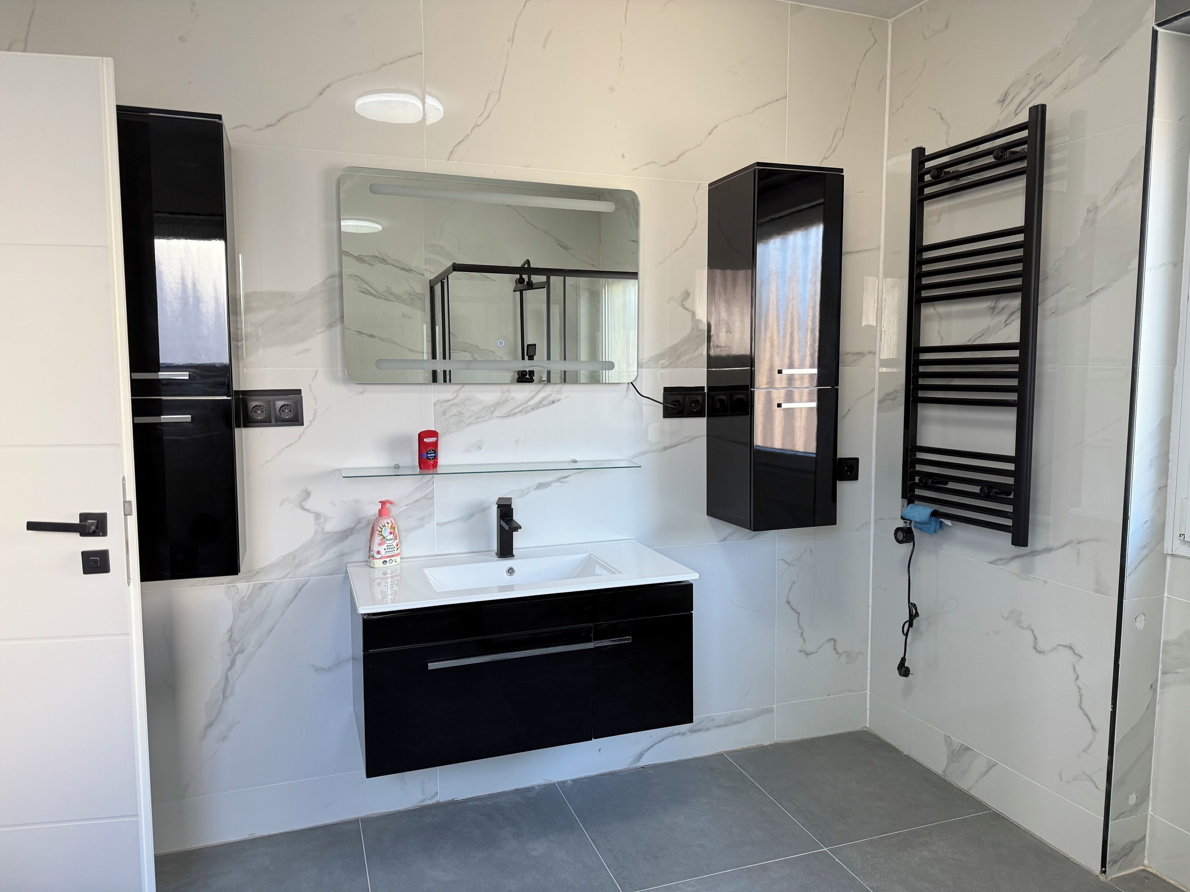 A modern bathroom with a white marble sink, black cabinetry, a glass shelf, and a towel rack.