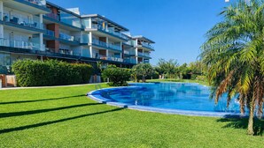 A swimming pool surrounded by well-maintained grass, with a multi-story building in the background. - At469 in Oliva With 2 Bedrooms and 2 Bathrooms (Oliva)