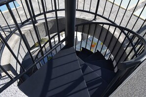Eine Wendeltreppe mit Metallgeländer, die zu einem Raum mit einem weißen Tisch und Stühlen führt.