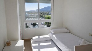 A single-bed room with a large window, a small table, and a wicker basket. - At469 in Oliva With 2 Bedrooms and 2 Bathrooms (Oliva)