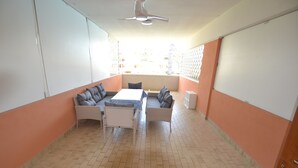 Una habitación con piso de baldosas, ventilador de techo, un conjunto de sofás y una mesa.