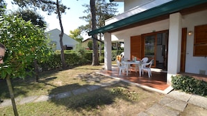 A covered patio with outdoor furniture, a stone pathway, and a well-maintained garden. - Two-level flat with garden and pool (Bibione)