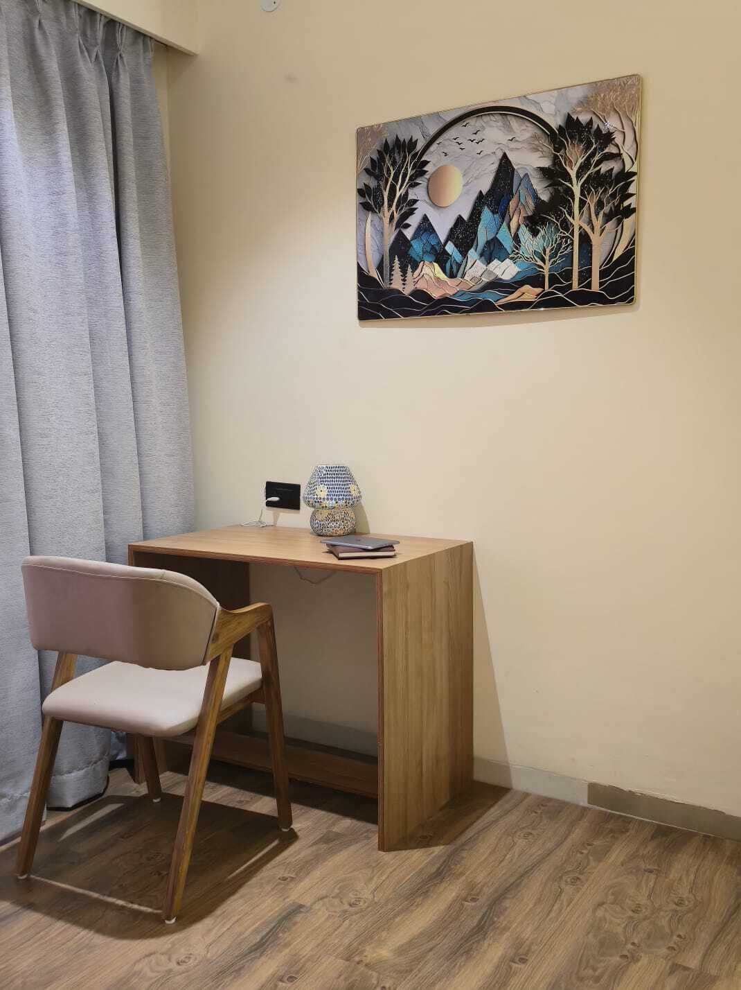 Una stanza con una scrivania in legno, una sedia, un quadro appeso al muro e una finestra con tende.