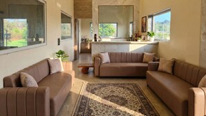 A spacious living room with a large window, a marble backsplash, and a modern ceiling fan. - Saapna Resort & Boat Club (Betūl)