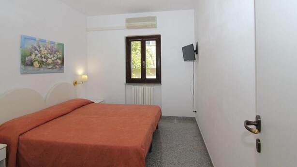 Een kamer met een bed, een radiator, een raam en een schilderij aan de muur.