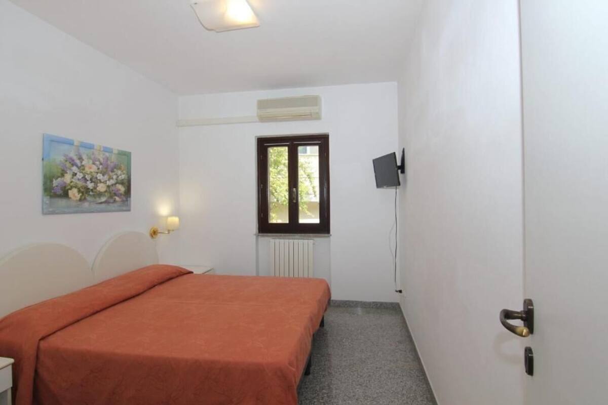 A room with a bed, a radiator, a window, and a painting on the wall.