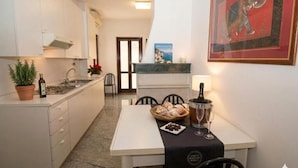 Een compacte keuken met witte kastjes, een eettafel met een zwarte tafelkleed en een ingelijste foto aan de muur.