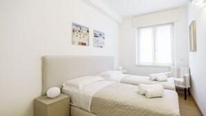 Quarto de hotel com duas camas, uma janela e uma cadeira.