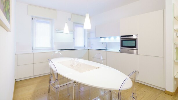 Uma cozinha moderna com armários brancos, uma mesa de jantar branca e luminárias pendentes.