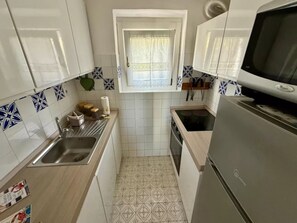 A compact kitchen with white cabinets, a stainless steel sink, a microwave, and patterned floor tiles. - Stunning sea view in a private setting (Stintino)
