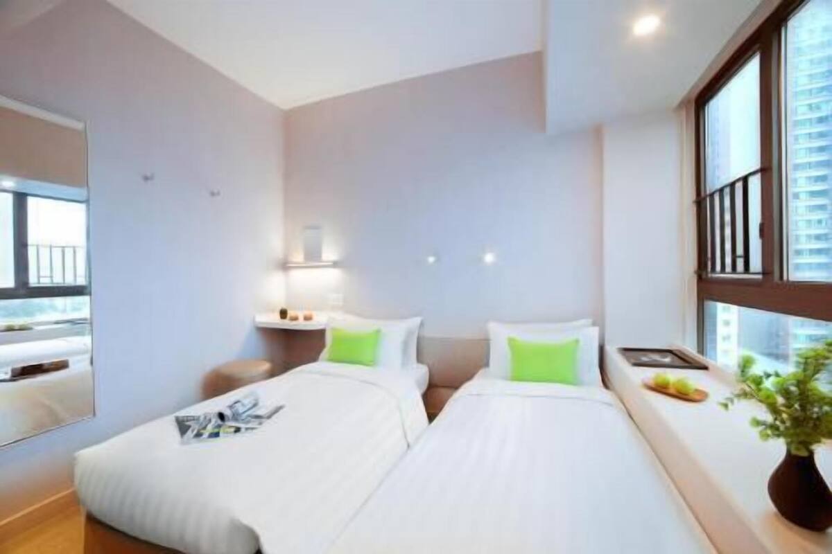 Habitació d'hotel amb dos llits, una taula petita, una meseta de nit, una finestra amb vista i una planta en test.