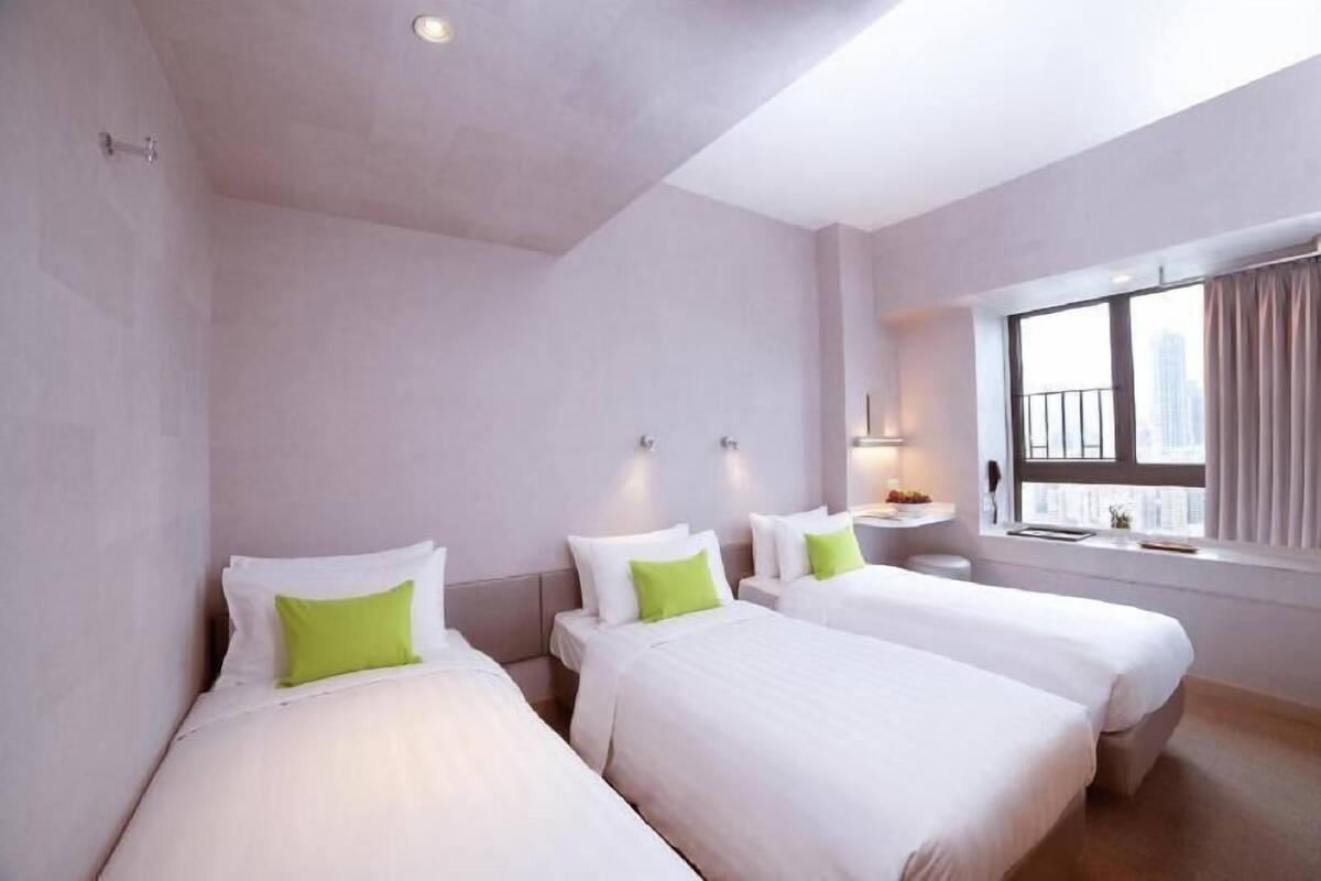 Habitació d'hotel amb dos llits, una finestra amb cortines, una taula de nit amb una làmpada i vista a la ciutat.