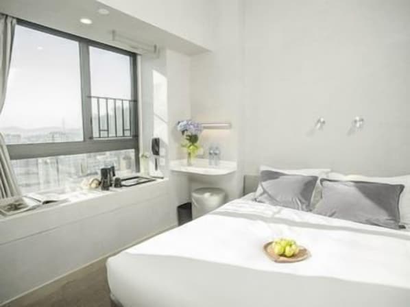 A hotel room with a large bed, a bedside table with a vase of flowers, a window with a view, and a small bathroom area.