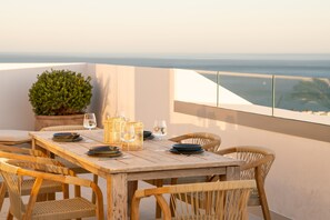 A wooden table set with plates, glasses, and wicker baskets on a balcony overlooking the sea. - Panorama Luxury Penthouse in Higueron (Benalmádena)