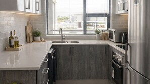 Una cocina moderna con gabinetes grises, electrodomésticos de acero inoxidable y un ventanal que proporciona luz natural.