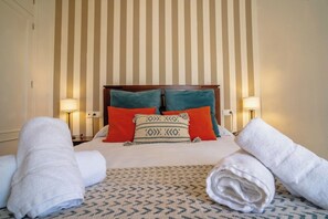 Ein Hotelzimmer mit einer gestreiften Wand, einem Holzkopfende, zwei Kissen, zwei Nachttischlampen und zusammengerollten Handtüchern auf dem Bett.