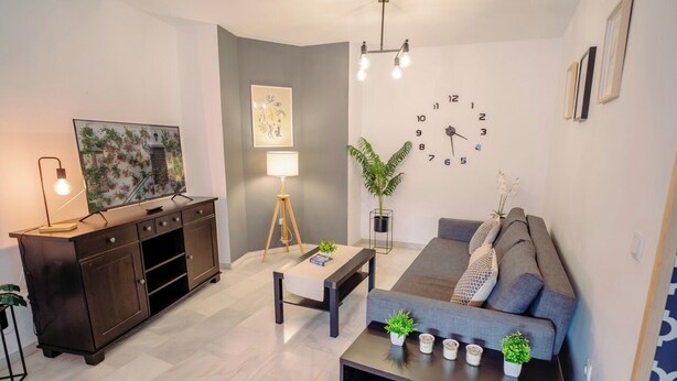 Een moderne woonkamer met een bank, salontafel, televisie en een wandklok.