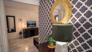 Een moderne woonkamer met behang met een patroon, een grote spiegel, een groene bank en een televisie.