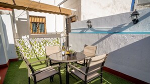 Een ronde tafel met vier stoelen, een glazen plank en een potplant op een terras met kunstgras.