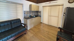 A compact living space with a sofa, a kitchen area with a tiled backsplash, and a large window with blinds. - Bluewoods Homestay – Serene Retreat Near Kochi City (Ernakulam)