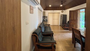 A spacious room with a long wooden bench, a ceiling fan, and a large window. - Bluewoods Homestay – Serene Retreat Near Kochi City (Ernakulam)