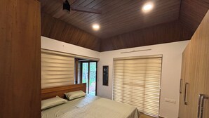 A bedroom with a wooden ceiling, a large bed with a quilted bedspread, a window with blinds, and a wardrobe. - Bluewoods Homestay – Serene Retreat Near Kochi City (Ernakulam)
