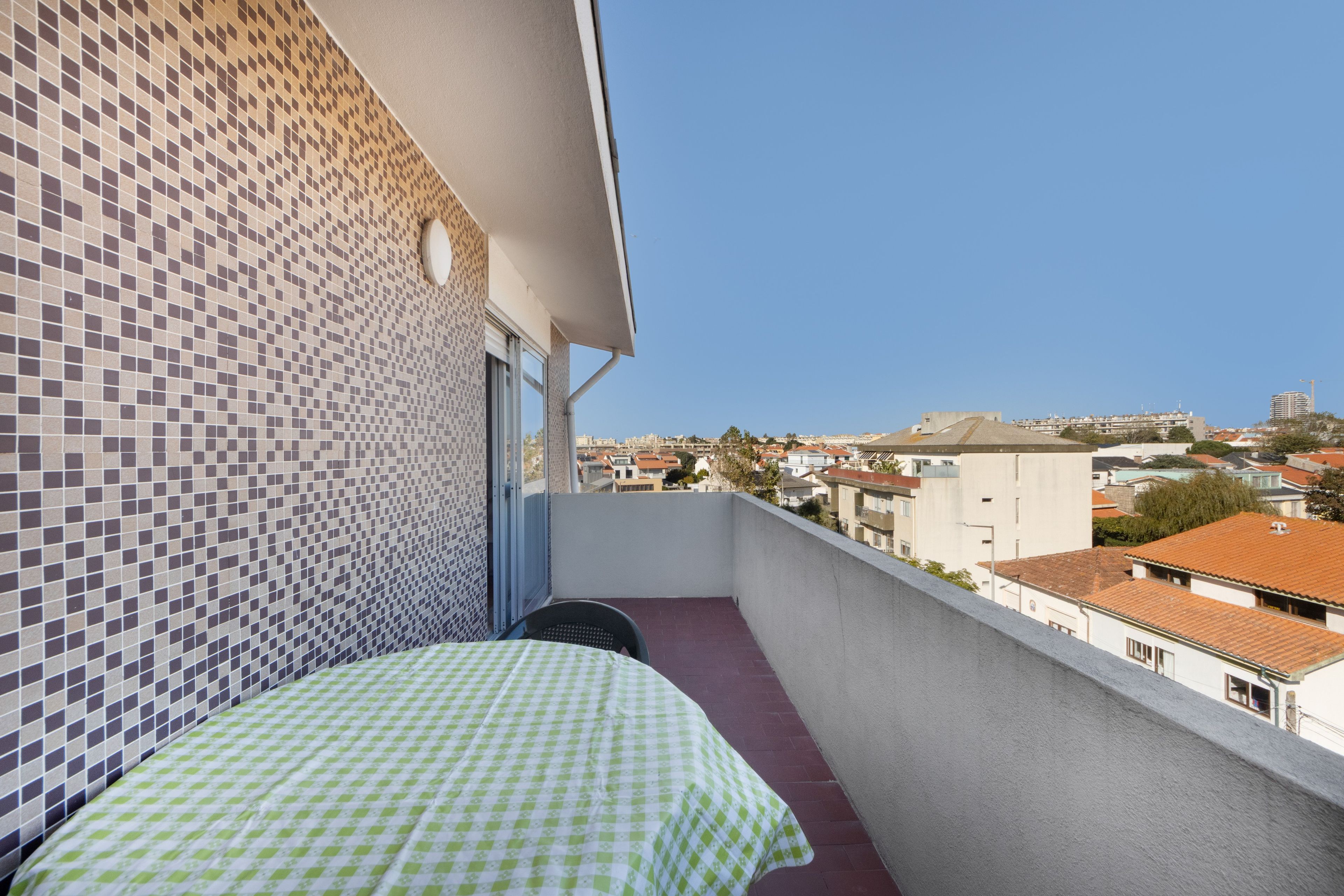 Un balcón con mantel a cuadros, pared de azulejos y vistas a la ciudad.
