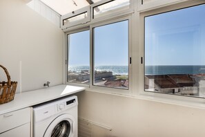 A laundry room with a washing machine, a drying rack, and a view of the sea through large windows. - Holiday Home 'Sunshine Home - 300m To The Beach' with Sea View, Private Terrace and Wi-Fi (Leça da Palmeira)