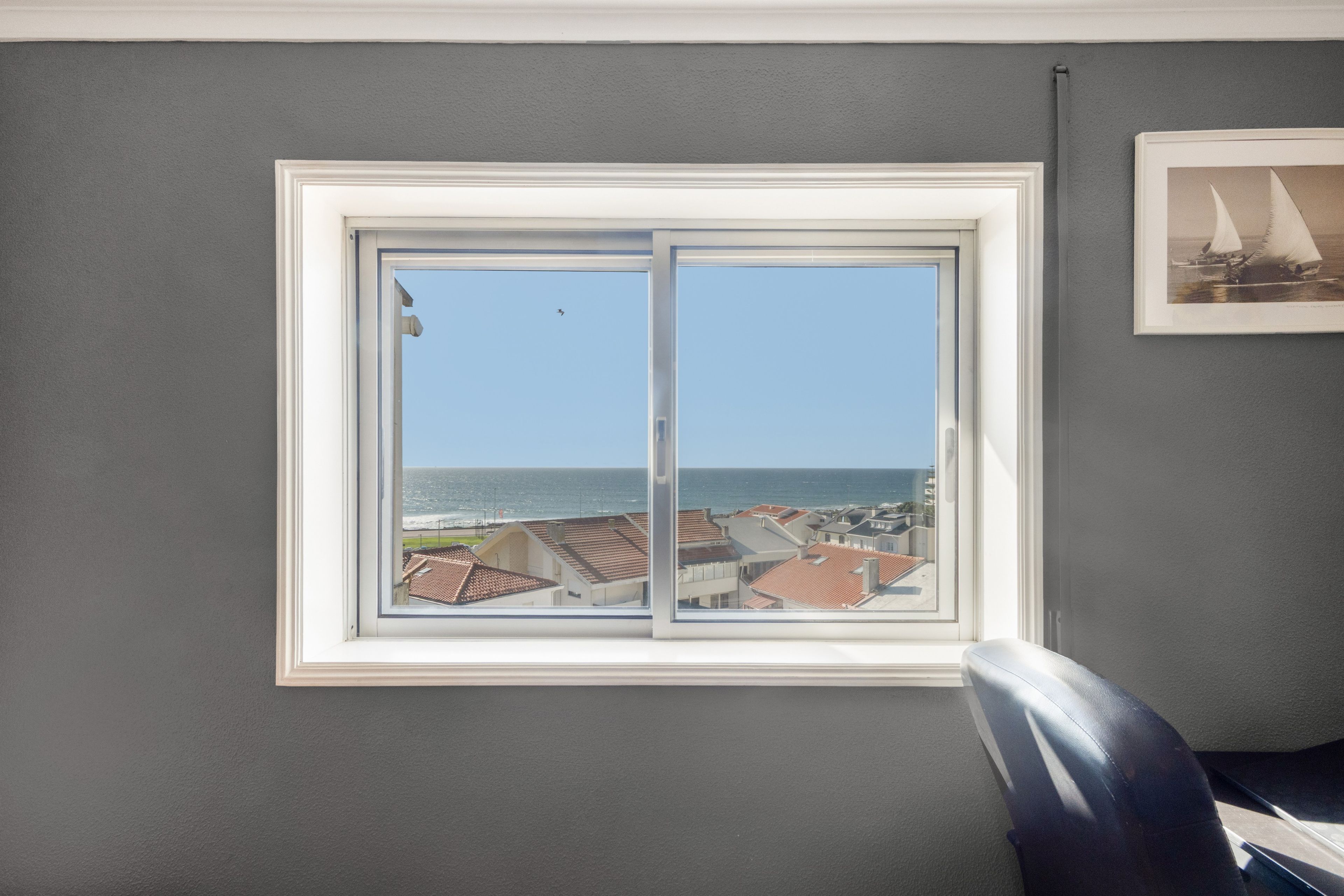 Habitación con un amplio ventanal con vistas al litoral, un cuadro en la pared y una silla.