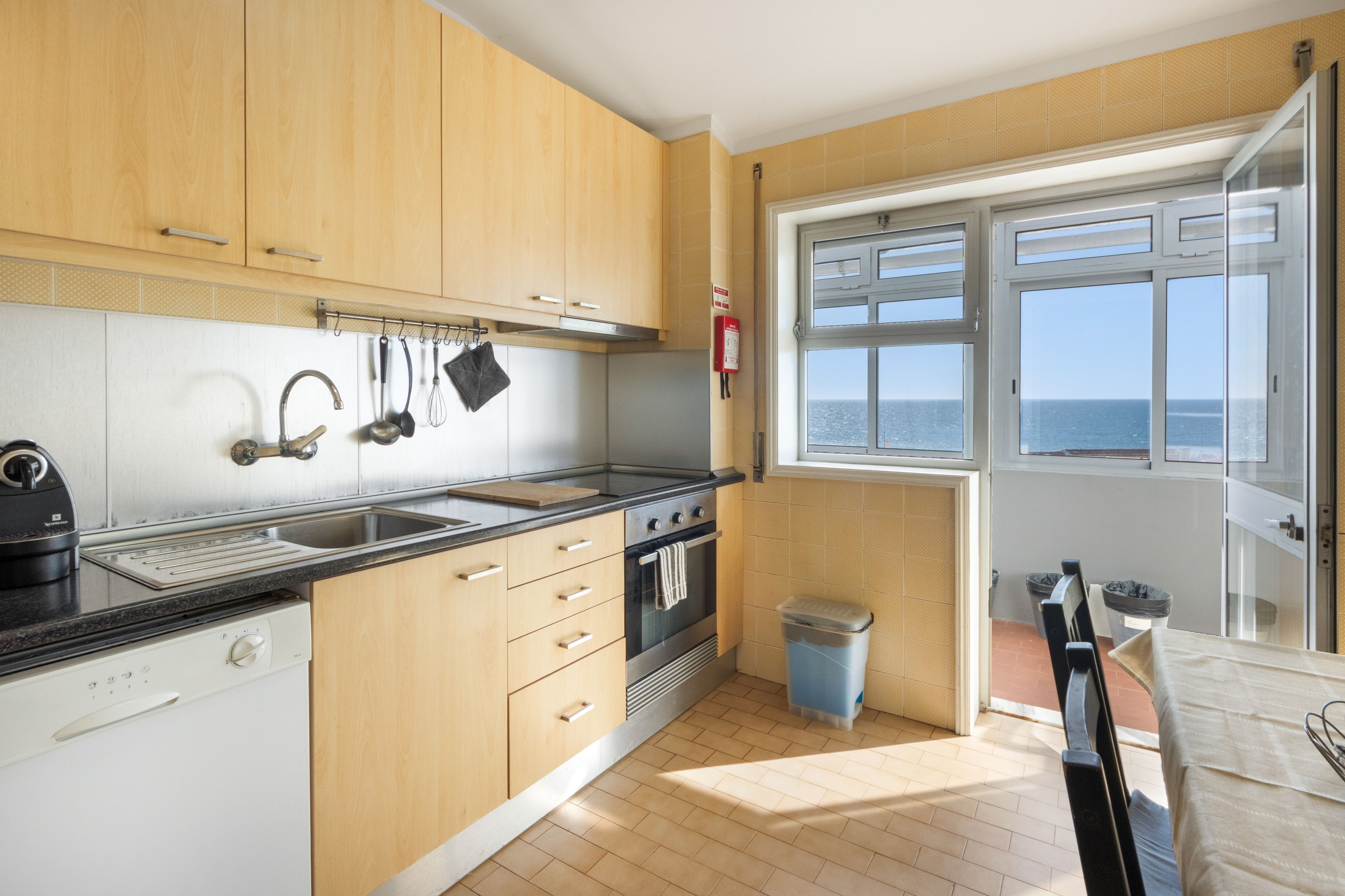 Una cocina moderna con armarios de madera, un lavamanos de acero inoxidable y un horno. Hay una ventana con vista al mar.