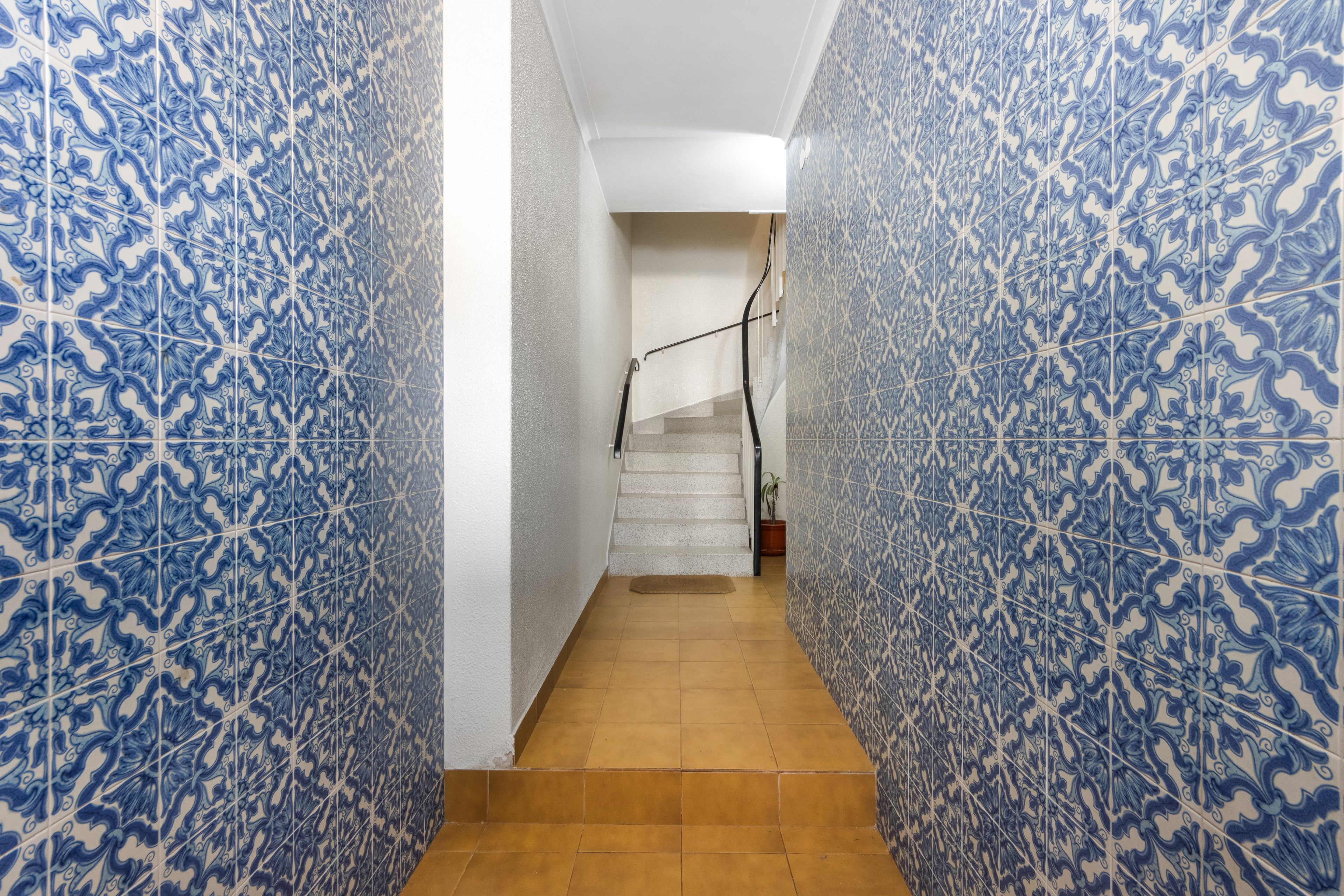 Un pasillo con baldosas azules estampadas en las paredes y un suelo de madera que conduce a una escalera.