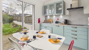 A modern kitchen with light blue cabinets, a white dining table set with bowls and cups, and a view of the backyard through a glass door. - House for 6 with garden, St Gildas town centre (Saint-Gildas-de-Rhuys)